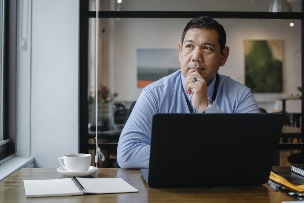 Thoughtful ethnic businessman using laptop while working in office